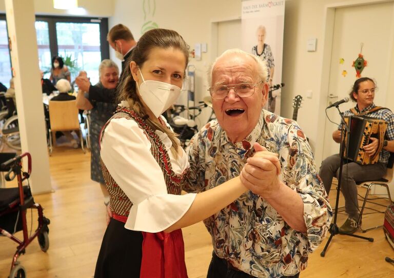Eine Mitarbeiterin im Dirndlkleid tanzt mit einem Bewohner. Sie hat ein Dirndl an. Es handelt sich um ein Oktoberfest
