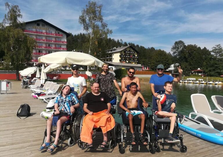 Kund*innen und Mitarbeiter*innen stehen für ein Gruppenbild auf einer Brücken neben dem See zusammen.