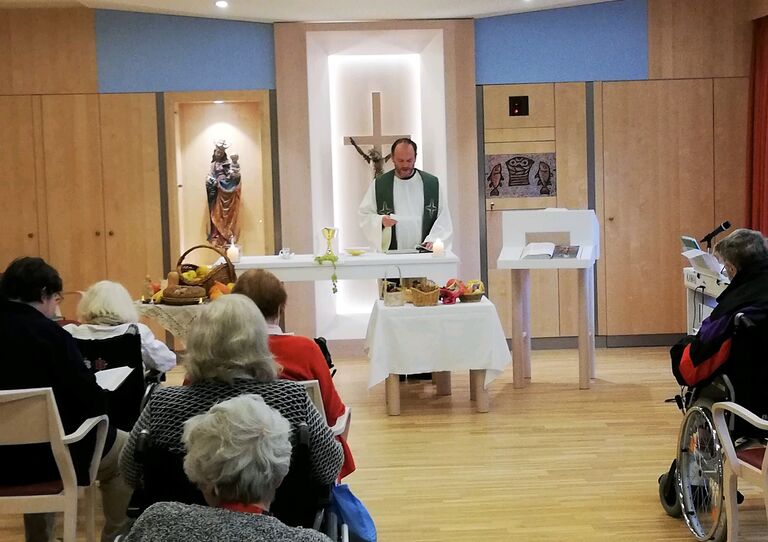 Bewohnerinnen und Bewohner feiern im Festsaal die heilige Messe mit Pfarrer Harald.