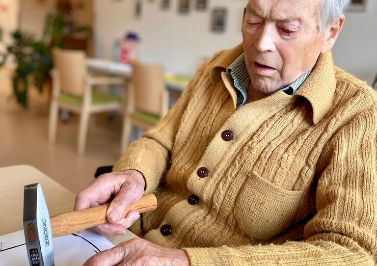 Bewohner hält Hammer und klopft damit auf ein Bild