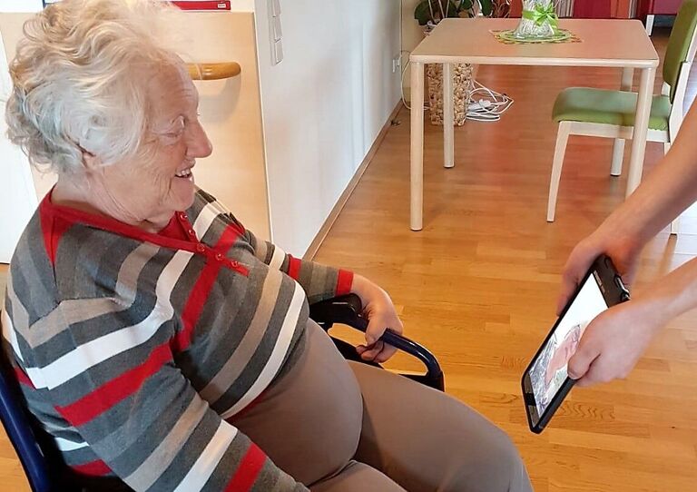 Eine Mitarbeiterin hält das Tablet für eine Bewohnerin.