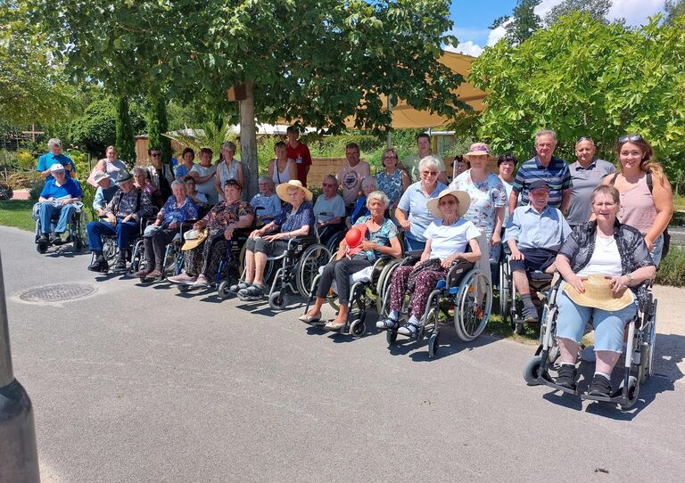 18 Bewohner*innen und einige HB Mitarbeiter*innen stehen für ein Gruppenbild zusammen.