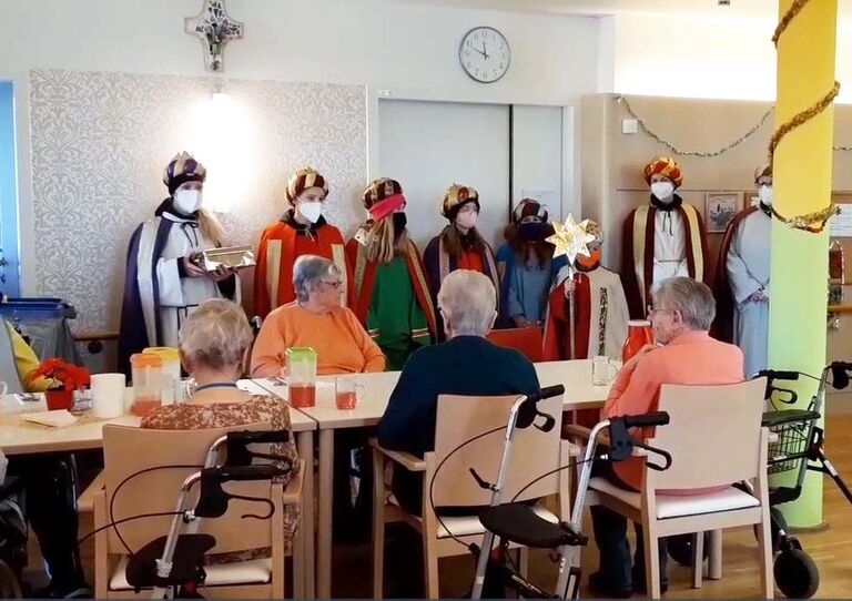 Sternsinger singen und die Bewohner*innen an den Tischen hören aufmerksam zu.