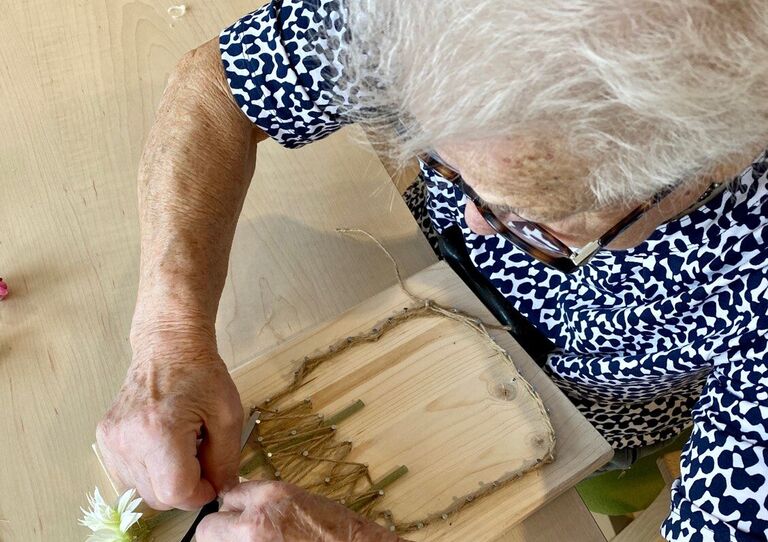 Aufnahme von oben. Bewohnerin steckt Blumen in das Bild.