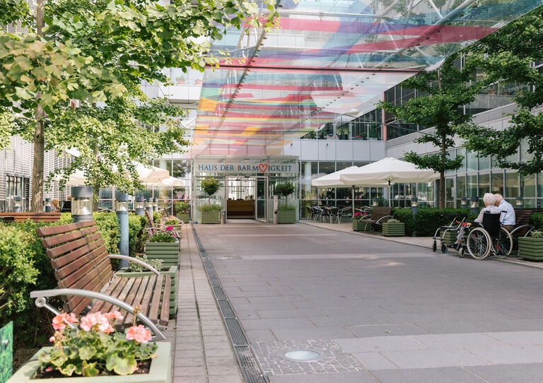 Eingang vom Pflegekrankenhaus Seeböckgasse mit buntem Glas-Vordach und Bank im Vordergrund. 