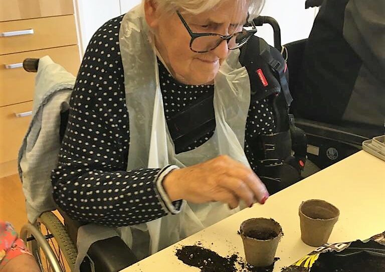 Eine Bewohnerin streut Samen in einen Topf.