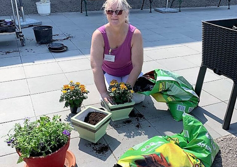 Eine Mitarbeiterin des Stadtheims Wiener Neustadt pflanzt Blumen in Töpfe.
