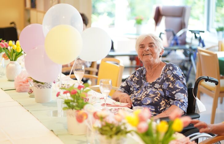 Eine Bewohnerin sitzt an einem festlich dekorierten Tisch, die Deko ähnelt einer eleganten Gartenparty