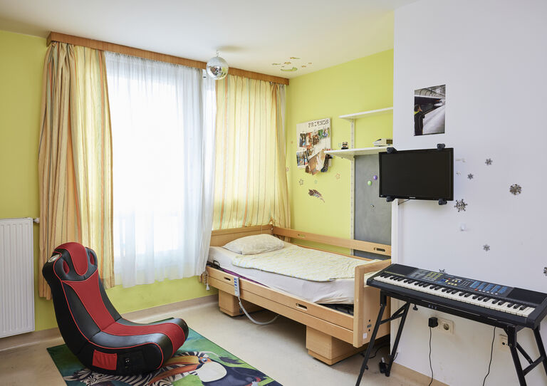 Kund*innen-Zimmer der HABIT WG Kulmgasse mit Pflegebett, Schaukelstuhl und Keyboard