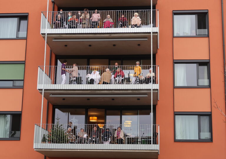 Nahaufnahme von den Bewohner*innen auf den Balkonen, sie sind dick eingepackt in Jacken und Decken.