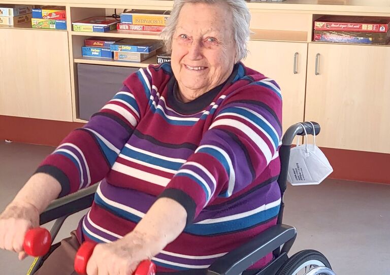 Bewohnerin trainiert mit Hantel und blickt in die Kamera.