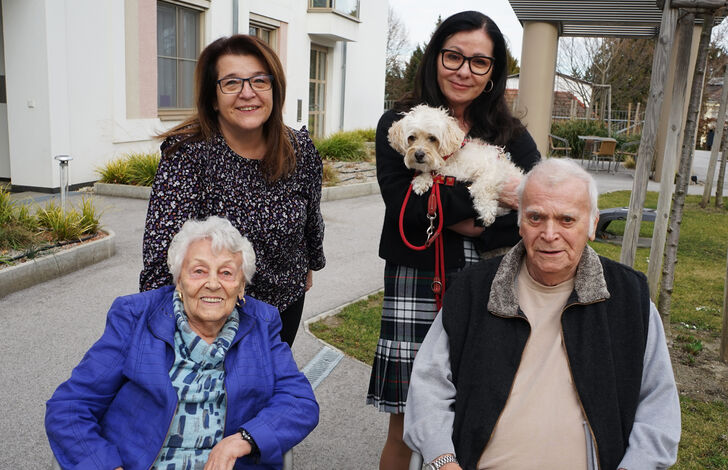 Vorne eine Bewohnerin und ein Bewohner im Rollstuhl. Hinten Andrea Jarosch und Christa Hock mit Hund