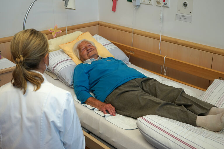 Eine Bewohnerin liegt am Bett und wird von der Ärztin in einen hypnotischen Zustand versetzt.