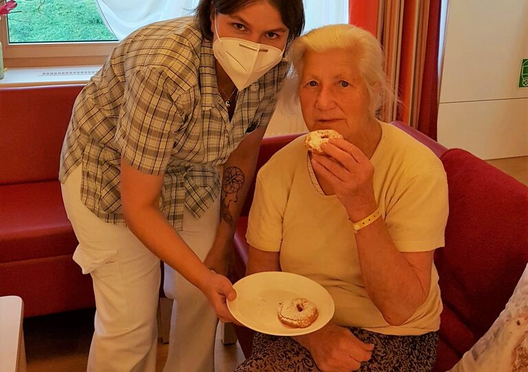 Eine Bewohnerin genießt die fertigen Apfelringe, die die Mitarbeiterin ihr gebracht hat.
