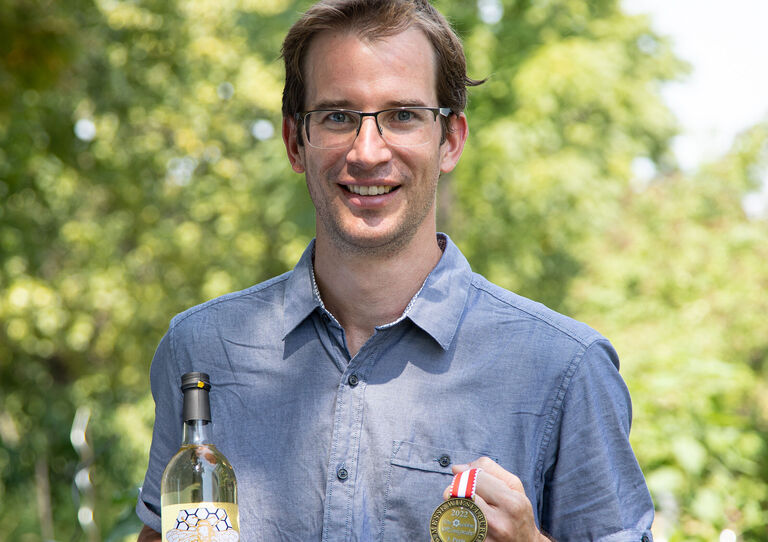 Florian Lackinger hält eine Medaille und eine Flasche seines Mets in die Kamera.