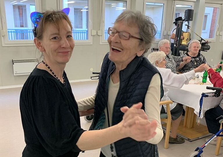 Eine verkleidete Mitarbeiterin und eine lachende Bewohnerin wagen ein Faschingstänzchen.