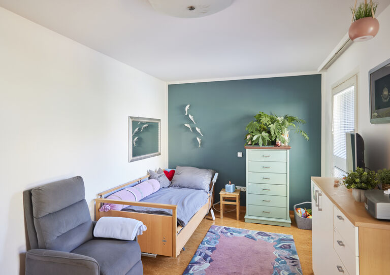 WG Otto-Herschmann-Gasse individuelles Kund*innen-Zimmer mit Pflegebett, hellgrüner Kommode und einer dunkelgrünen Wand