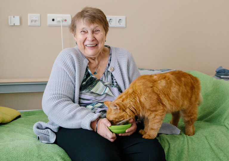 Bewohnerin Maria füttert Kater Stephan auf ihrem Bett.