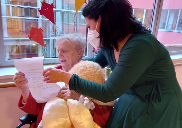 Bewohnerin Elsa schaut eine kleine Schutzengelpuppe an, die ihr Mitarbeiterin Daniela überreicht.