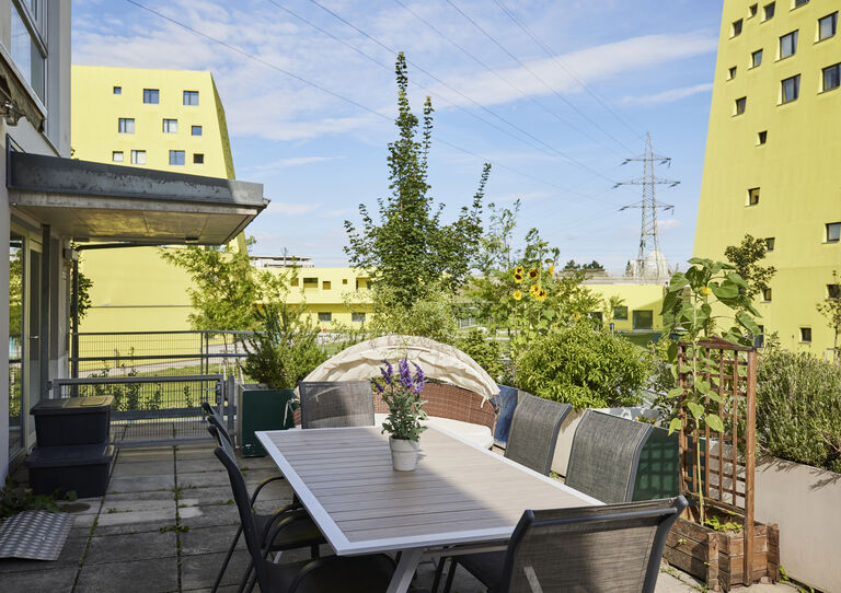 Terrasse der HABIT WG Perfektastraße mit Gartenmöbeln, Pflanzen und großen gelben Wohnhäusern im Hintergrund