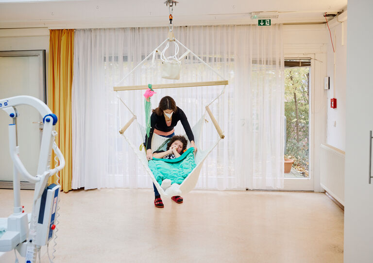 BTZ Maria-Rekker-Gasse: Kundin in der Hängematte wird von Betreuerin geschaukelt.