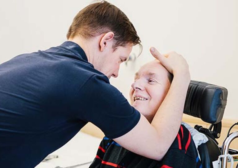 Physiotherapeut Daniel Preiser streicht Bewohner Paul Lederbauer über das Gesicht.