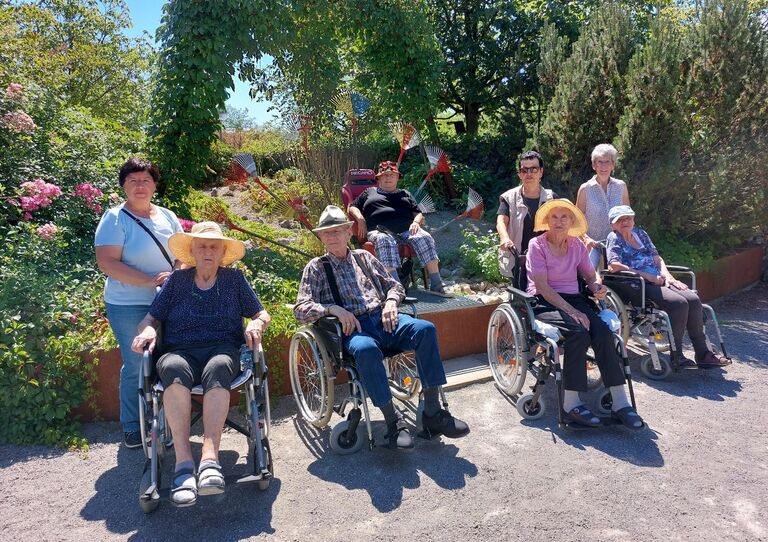 Vier Bewohner*innen im Rollstuhl sitzen nebeneinander und dahinter stehen ihre jeweiligen Begleiter*innen