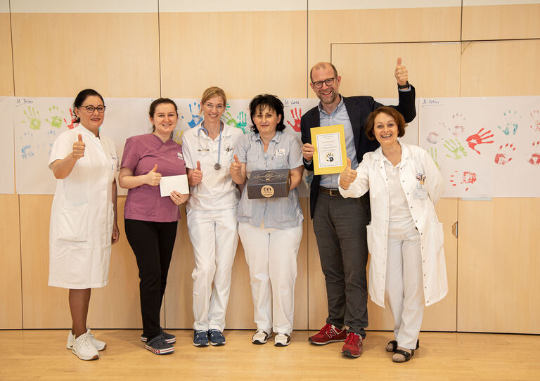 Einige Kolleg*innen stehen vor einem Transparent zusammen und halten ihre Hände hoch