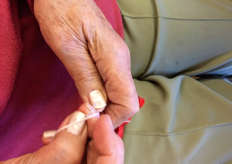 Die Hände einer Bewohnerin, die einen Anhänger bastelt, in Nahaufnahme.