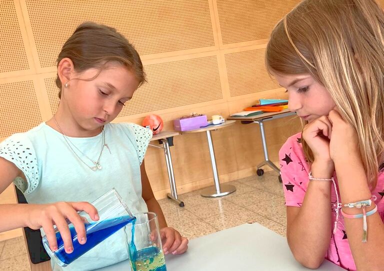 Zwei Mädchen schütten eine blaue Flüssigkeit in ein Glas.