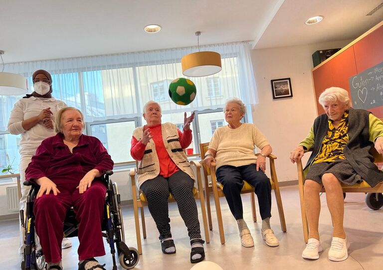 Vier Bewohner*innen sitzen im Sesselkreis und spielen mit einem Ball.