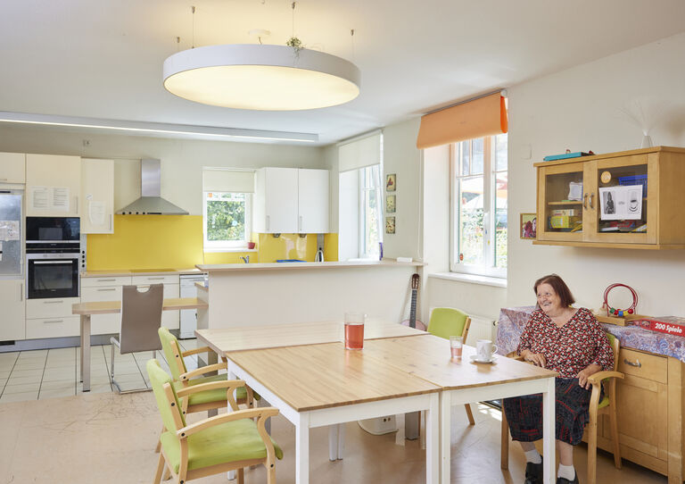 Kundin sitzt bei Tisch im großen Wohnzimmer der HABIT WG Oswaldgasse