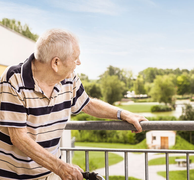Ein Bewohner schaut vom Balkon ins Grüne.