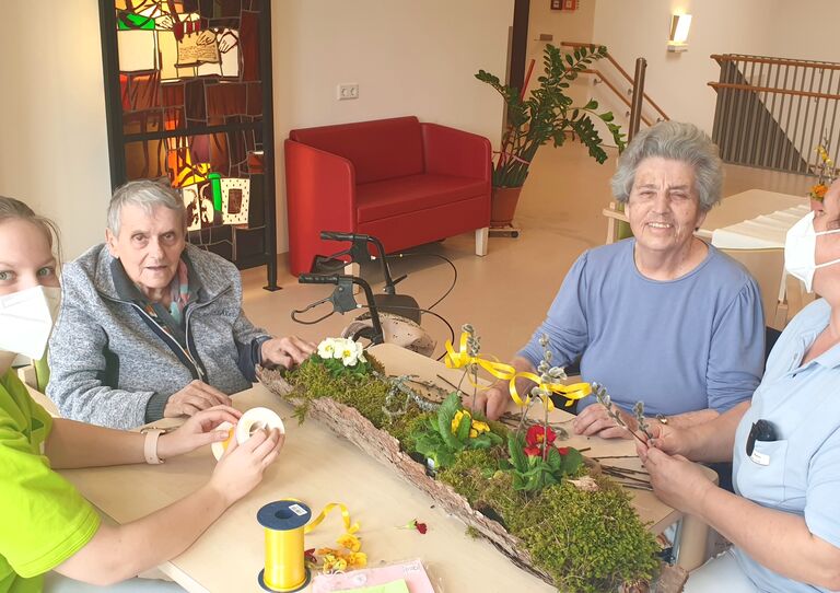 Zwei Bewohner*innen und und Mitarbeiter*innen basteln das Ostergesteck.