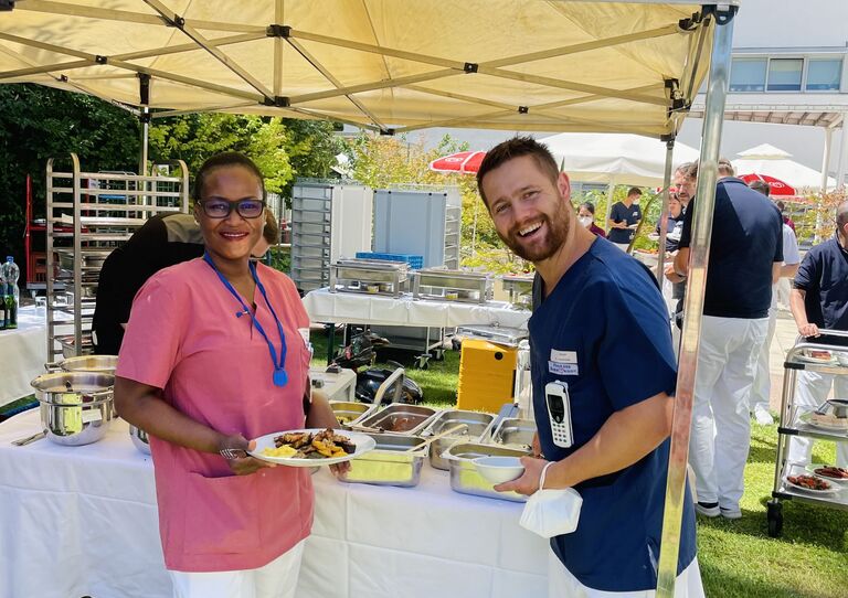 Eine Kollegin und ein Kollege stehen outdoor bei der Essensausgabe an.