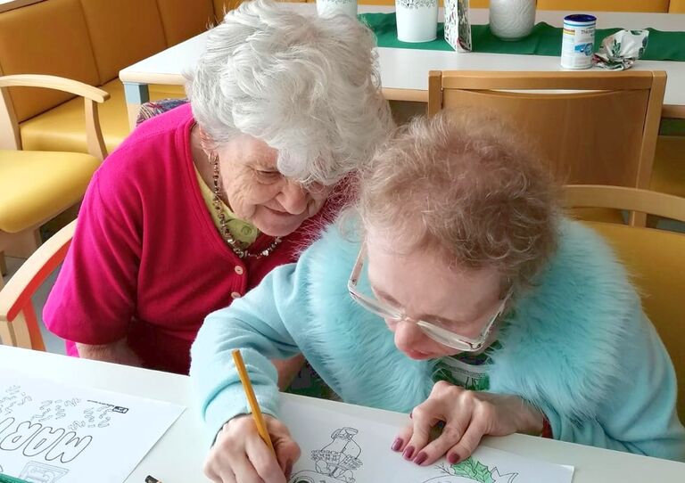 Zwei Bewohnerinnen sitzen nebeneinander am Tisch und malen ein Ausmalbild