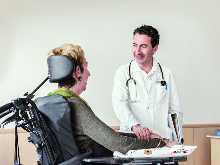 Arzt hält Bewohnerin im Rollstuhl an den Händen