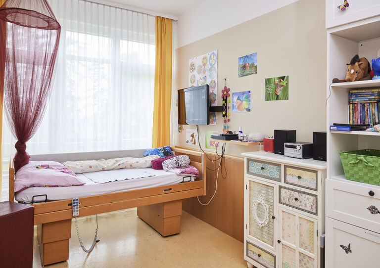Kund*innen-Zimmer mit Pflegebett, Kommode und Regal in der HABIT WG 2 Clementinum