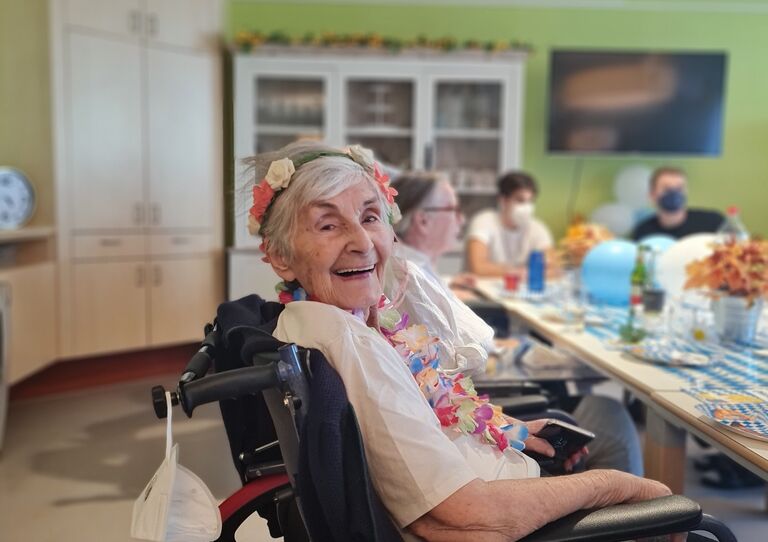 Eine Bewohnerin im Rollstuhl mit Blumenkranz im Haar lächelt in die Kamera