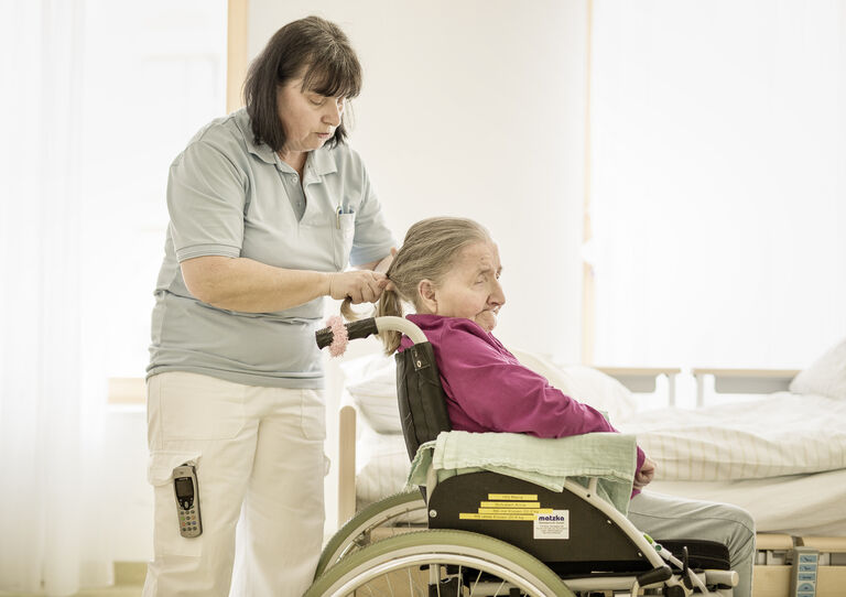Eine Pflegerin flechtet einer Bewohnerin einen Zopf.