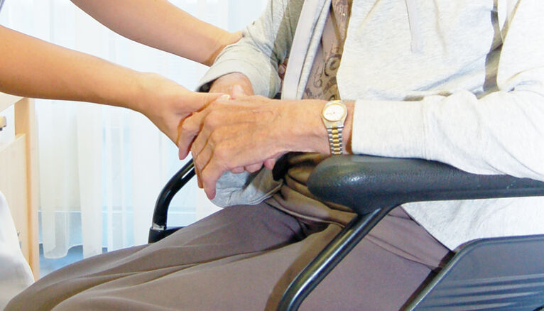Die Hände einer Pflegerin halten die Hände einer Bewohnerin.