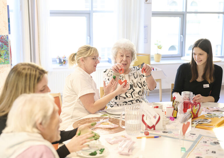 Studierende absolvieren das Praktikums. Sie sitzen gemeinsam mit Bewohner*innen um einen Tisch und führen Gespräche beim Basteln.  Studierende absolvieren das Praktikums. Sie sitzen gemeinsam mit Bewohner*innen um einen Tisch und führen Gespräche beim Basteln.