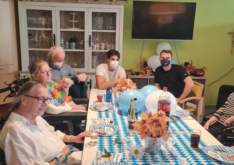 Einige Bewohner*innen sitzen an einer langen festlich dekorierten Tafel. 