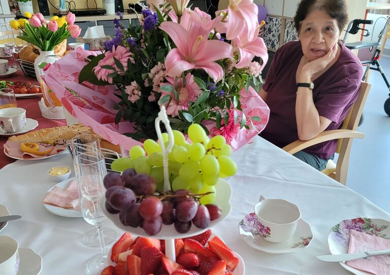 Bewohnerin schaut verträumt auf Blumenstrauß, vor ihr sind viele Früchte drapiert.