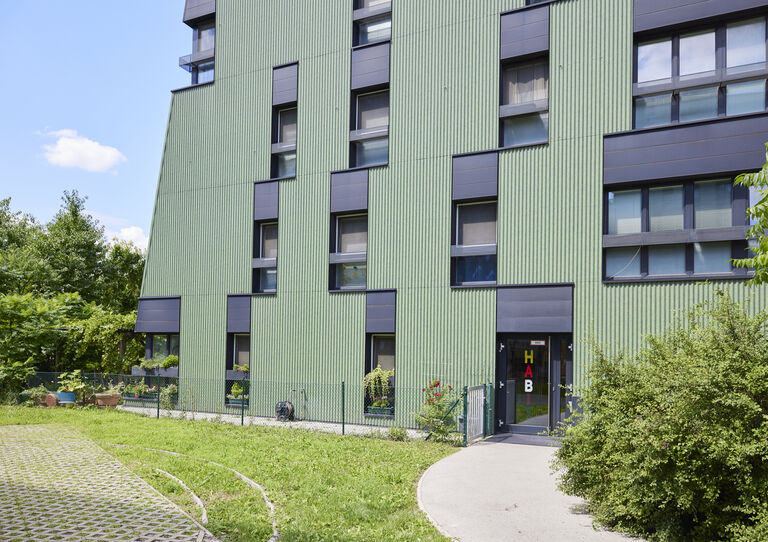 WG Otto-Herschmann-Gasse Außenansicht, grünes Gebäude mit Büschen im Vordergrund