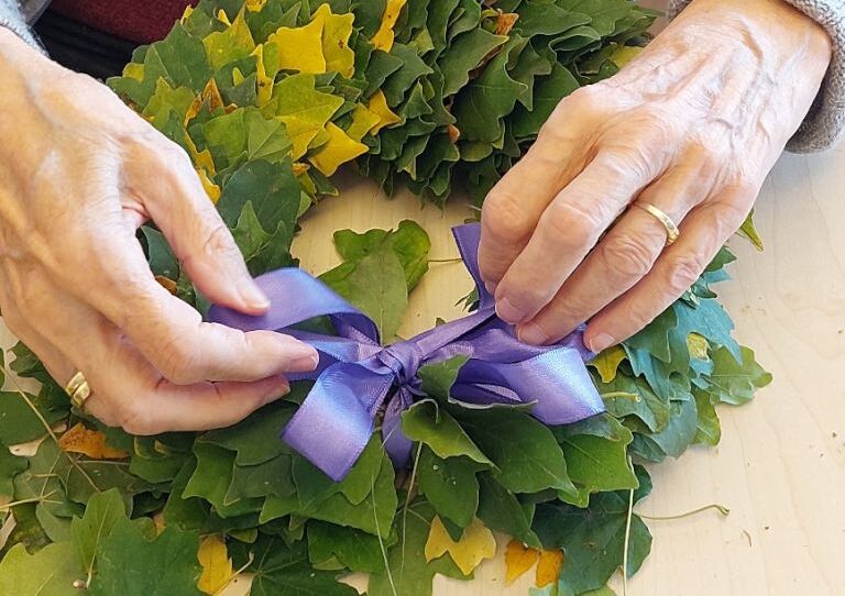 Aufnahme von Händen, die einen Laubkranz basteln.