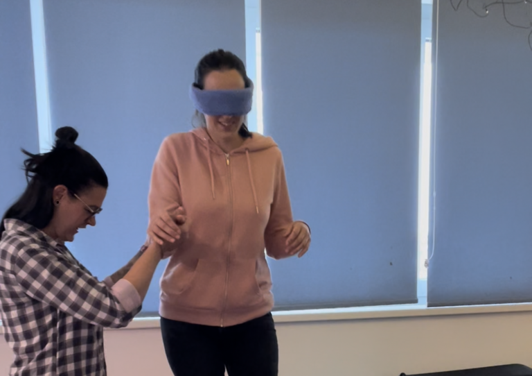 Besucherin geht mit eine Augenbinde mit Hilfe einer Mitarbeiterin am Hindernisparcours.