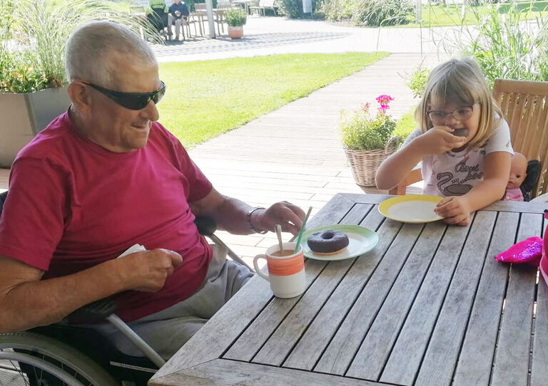 Haily Liv und ein Bewohner sitzen für eine Kaffejause am Tisch im Garten.