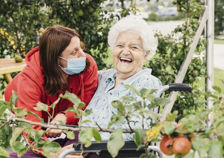 Bewohnerin Aloisia mit Mitarbeiterin unter einem Apfelbaum.
