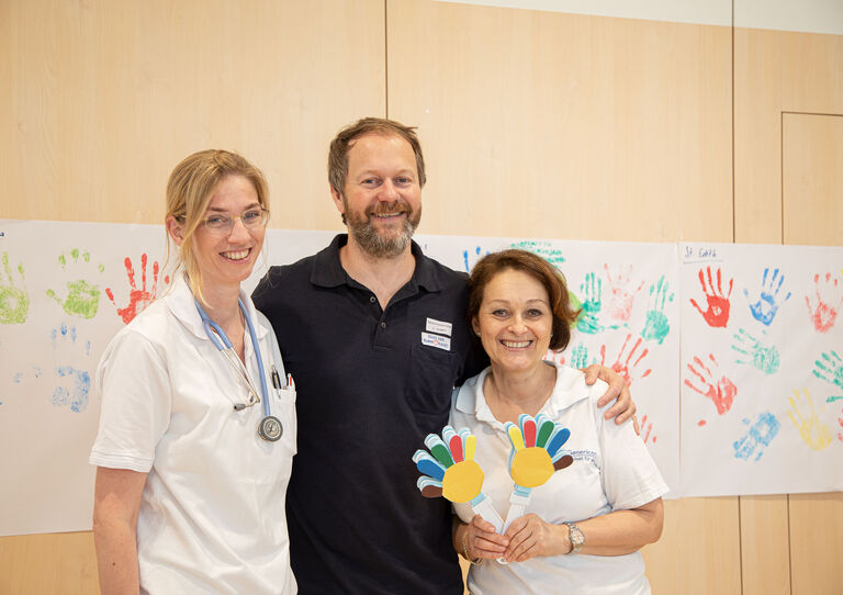 Drei Kolleg*innen vor einem Transparent mit Händen.